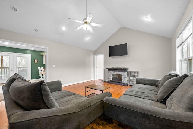 living room featuring a stone fireplace, high vaulted ceiling, wood-type flooring, ceiling fan, and french doors