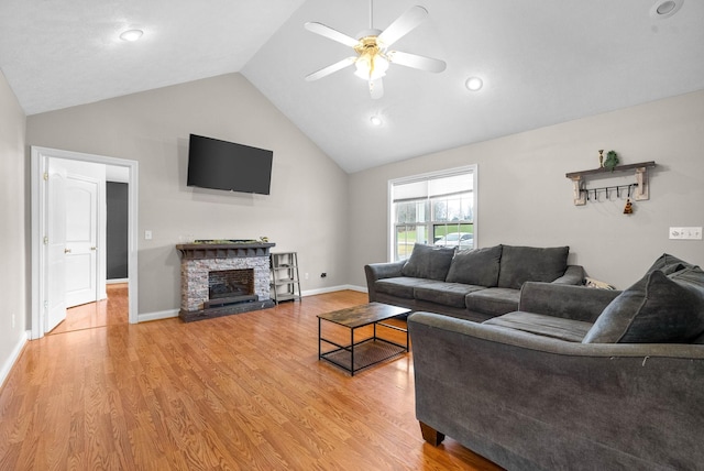 living room with vaulted ceiling, ceiling fan, a stone fireplace, and light wood-type flooring