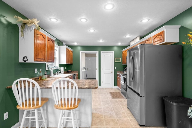 kitchen featuring a kitchen bar, sink, light tile patterned floors, appliances with stainless steel finishes, and kitchen peninsula