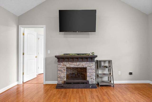 unfurnished living room with vaulted ceiling, a stone fireplace, and hardwood / wood-style floors