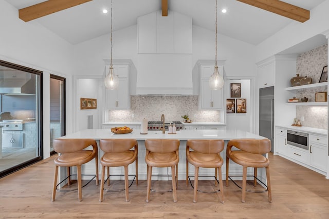 kitchen with white cabinetry, built in appliances, an island with sink, and decorative light fixtures