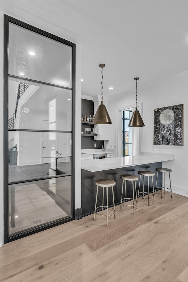 kitchen featuring decorative light fixtures, a kitchen bar, light hardwood / wood-style floors, kitchen peninsula, and crown molding