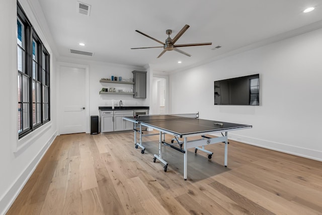 recreation room featuring ceiling fan, crown molding, indoor wet bar, and light hardwood / wood-style floors