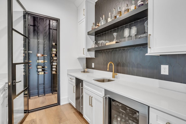 bar with sink, white cabinetry, wine cooler, tasteful backsplash, and light wood-type flooring