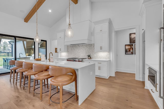 kitchen with decorative light fixtures, an island with sink, custom range hood, and white cabinets