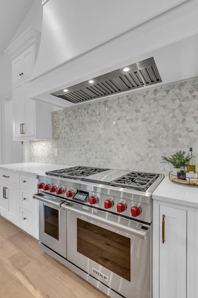 kitchen with light wood-type flooring, premium range hood, white cabinets, and range with two ovens