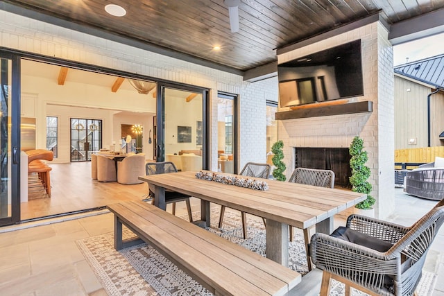 dining area featuring an outdoor brick fireplace, a healthy amount of sunlight, wooden ceiling, and beamed ceiling