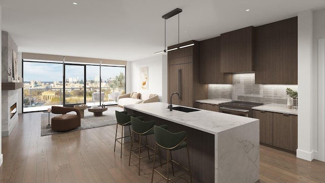 kitchen featuring pendant lighting, sink, a kitchen island with sink, tasteful backsplash, and a large fireplace