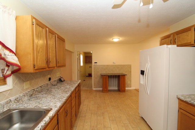 kitchen featuring tasteful backsplash, light stone counters, a textured ceiling, white refrigerator with ice dispenser, and light hardwood / wood-style floors