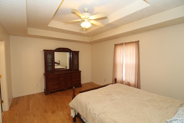 bedroom with ceiling fan, a tray ceiling, light hardwood / wood-style floors, and a textured ceiling