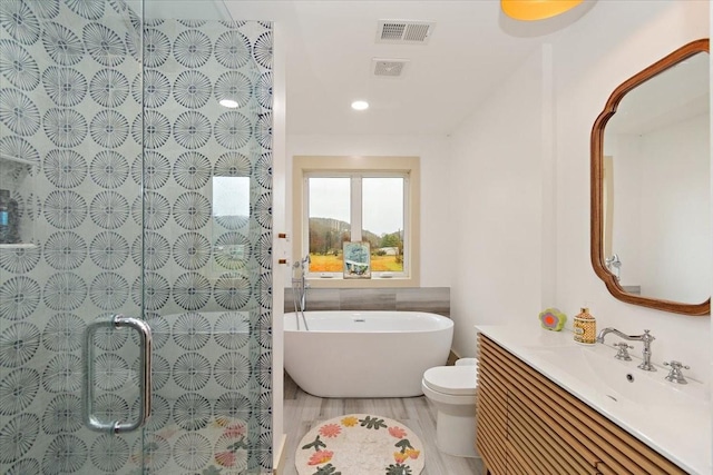 bathroom with visible vents, toilet, wood finished floors, vanity, and a freestanding tub