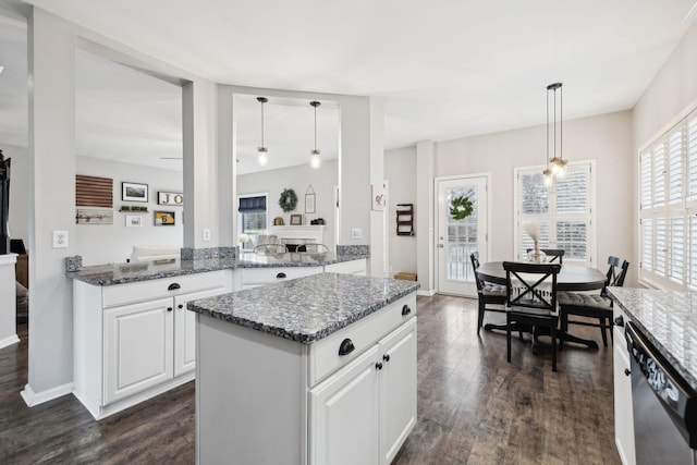 kitchen with white cabinetry, hanging light fixtures, stainless steel dishwasher, dark hardwood / wood-style floors, and dark stone counters