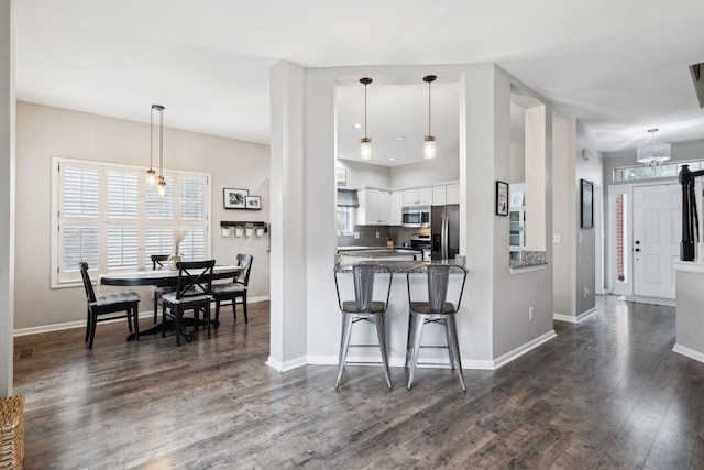 kitchen with hanging light fixtures, dark stone countertops, appliances with stainless steel finishes, kitchen peninsula, and white cabinets