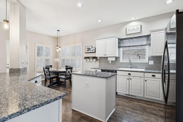 kitchen featuring black refrigerator, a kitchen island, pendant lighting, dark stone counters, and white cabinets