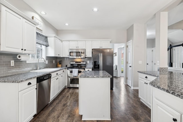 kitchen with appliances with stainless steel finishes, white cabinetry, sink, dark stone countertops, and a center island