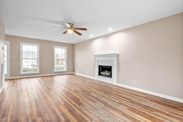 unfurnished living room featuring a premium fireplace, ceiling fan, and light wood-type flooring