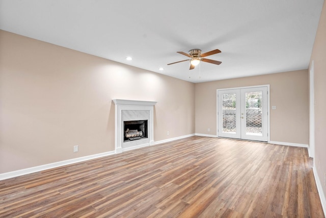 unfurnished living room featuring ceiling fan, hardwood / wood-style floors, a high end fireplace, and french doors