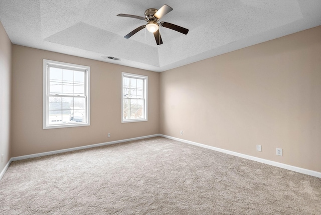 unfurnished room featuring ceiling fan, light colored carpet, a raised ceiling, and a textured ceiling