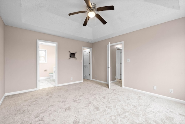 unfurnished bedroom featuring light colored carpet, ensuite bathroom, a raised ceiling, and a textured ceiling