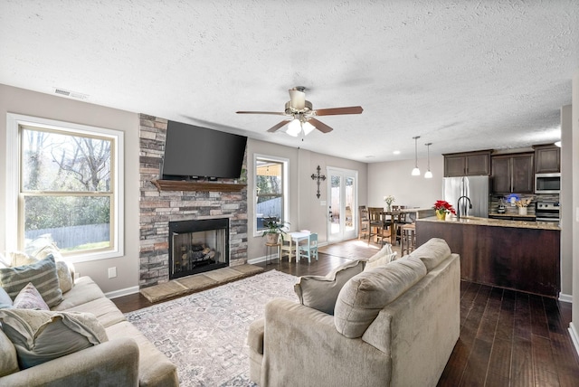 living room with a stone fireplace, dark wood-type flooring, a textured ceiling, and ceiling fan