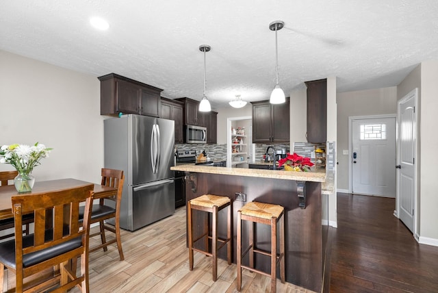 kitchen featuring appliances with stainless steel finishes, a breakfast bar area, backsplash, hanging light fixtures, and dark brown cabinetry