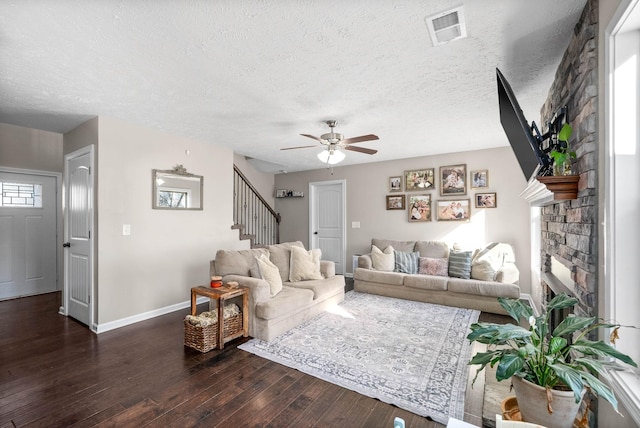 living room with ceiling fan, a stone fireplace, dark wood-type flooring, and a textured ceiling