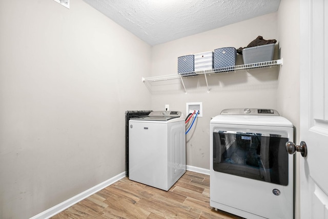 washroom featuring washing machine and clothes dryer, light hardwood / wood-style floors, and a textured ceiling