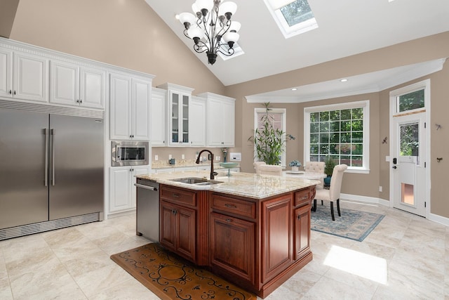 kitchen featuring decorative light fixtures, white cabinetry, an island with sink, sink, and built in appliances