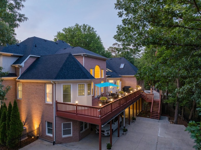 back house at dusk featuring a wooden deck and a patio area