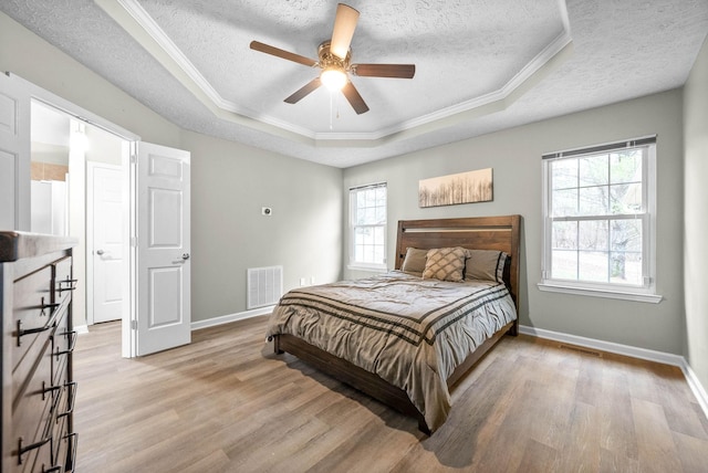 bedroom featuring light hardwood / wood-style flooring, a textured ceiling, ornamental molding, a raised ceiling, and ceiling fan