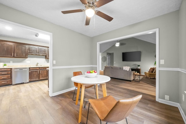 dining room with vaulted ceiling, sink, ceiling fan, light hardwood / wood-style floors, and a textured ceiling