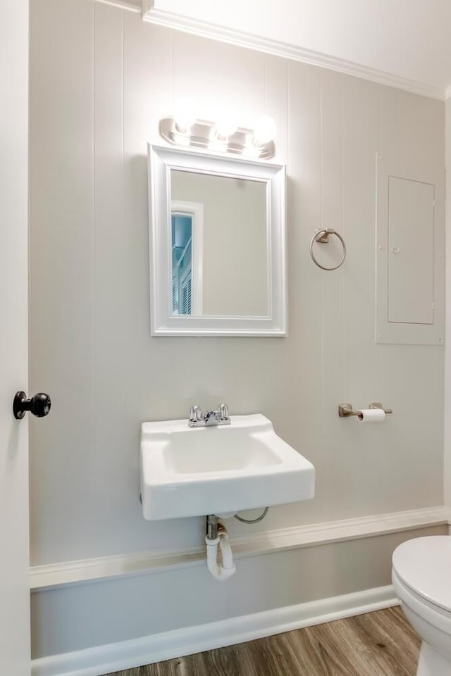 half bathroom with toilet, a sink, wood finished floors, ornamental molding, and electric panel