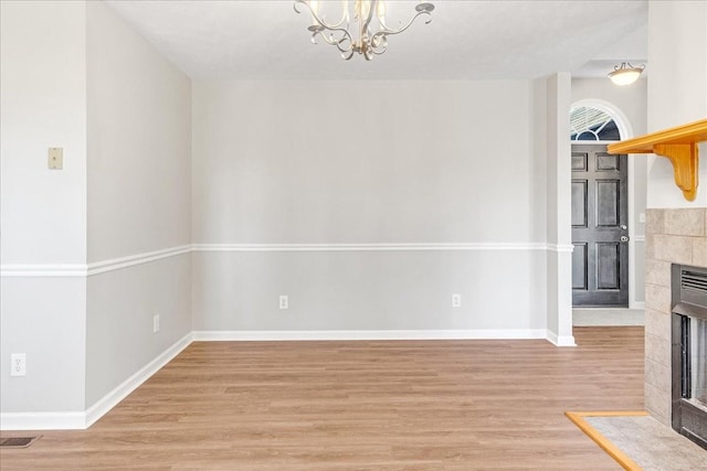 unfurnished living room featuring a tiled fireplace, light hardwood / wood-style floors, and an inviting chandelier