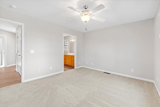 unfurnished bedroom featuring ceiling fan, ensuite bathroom, and light carpet