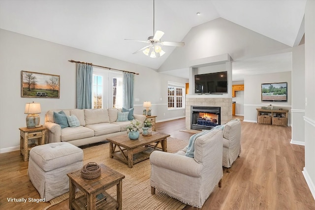 living room featuring high vaulted ceiling, a fireplace, light hardwood / wood-style floors, and ceiling fan