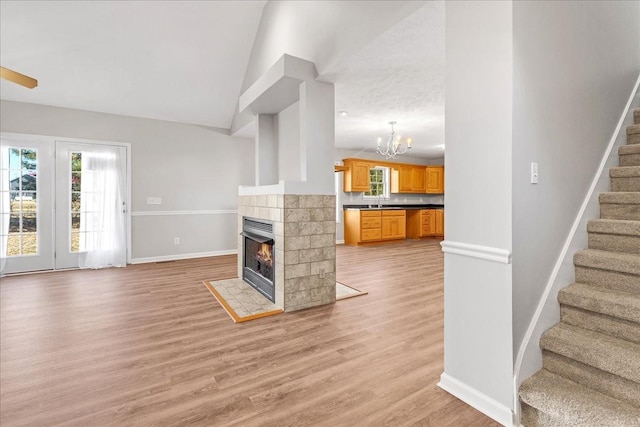 unfurnished living room with a tiled fireplace, a notable chandelier, and light hardwood / wood-style floors