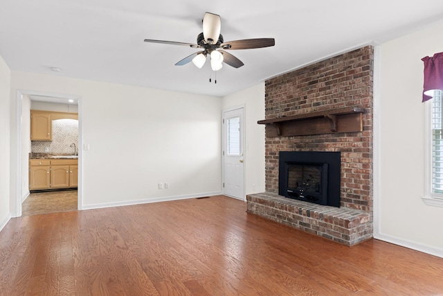 unfurnished living room featuring sink, a fireplace, light hardwood / wood-style floors, and ceiling fan