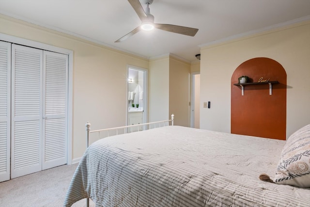 carpeted bedroom featuring crown molding, ceiling fan, ensuite bath, and a closet