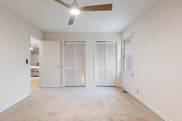 unfurnished bedroom with multiple closets, ceiling fan, and light carpet