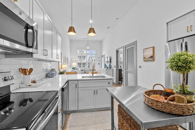 kitchen featuring pendant lighting, sink, appliances with stainless steel finishes, backsplash, and kitchen peninsula