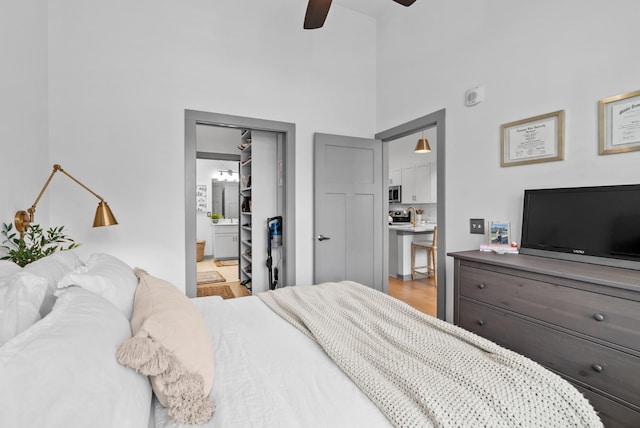 bedroom with ceiling fan, a towering ceiling, connected bathroom, and light hardwood / wood-style floors