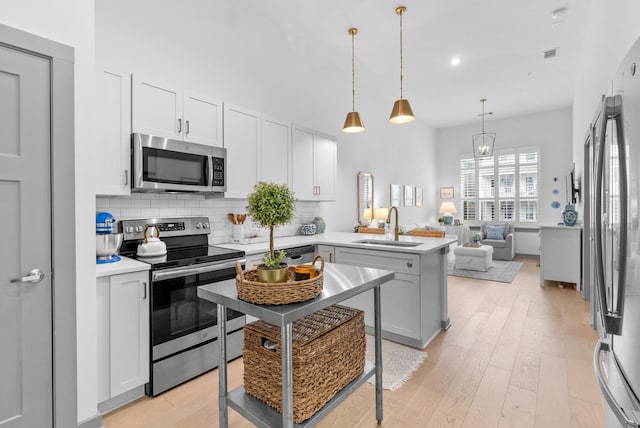 kitchen with pendant lighting, sink, backsplash, stainless steel appliances, and light wood-type flooring