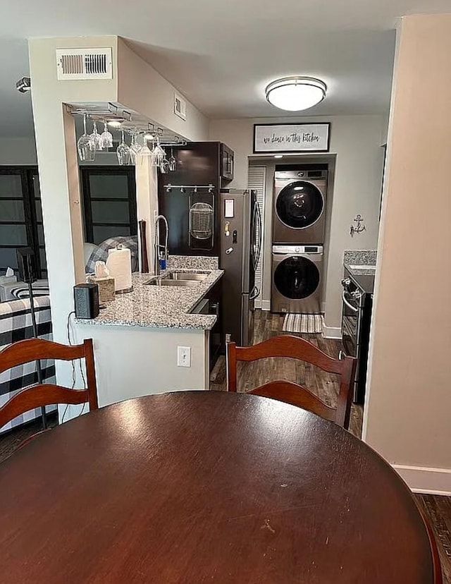 dining space featuring sink, stacked washer / drying machine, and dark wood-type flooring