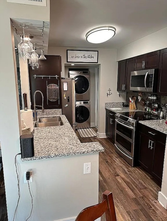 kitchen featuring sink, appliances with stainless steel finishes, light stone counters, stacked washer / drying machine, and dark hardwood / wood-style flooring