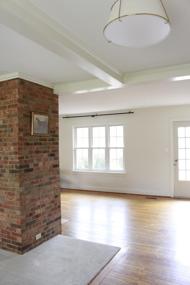 empty room featuring crown molding, beamed ceiling, brick wall, and light wood-type flooring