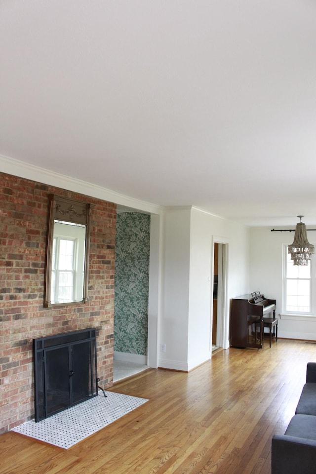 unfurnished living room with ornamental molding, a brick fireplace, a notable chandelier, and light hardwood / wood-style flooring