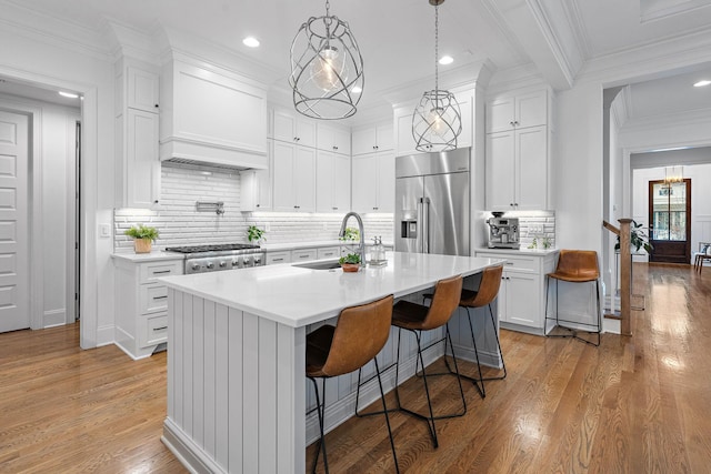 kitchen featuring built in refrigerator, a kitchen island with sink, hanging light fixtures, white cabinets, and a kitchen bar