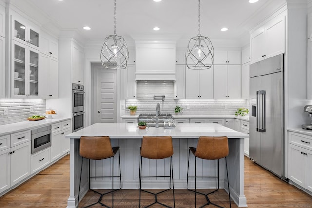 kitchen with a kitchen bar, built in appliances, an island with sink, and white cabinets