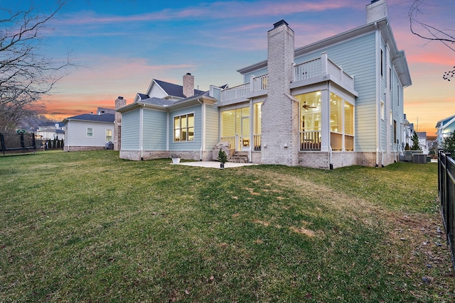 back house at dusk with a balcony, a patio area, a lawn, and central air condition unit