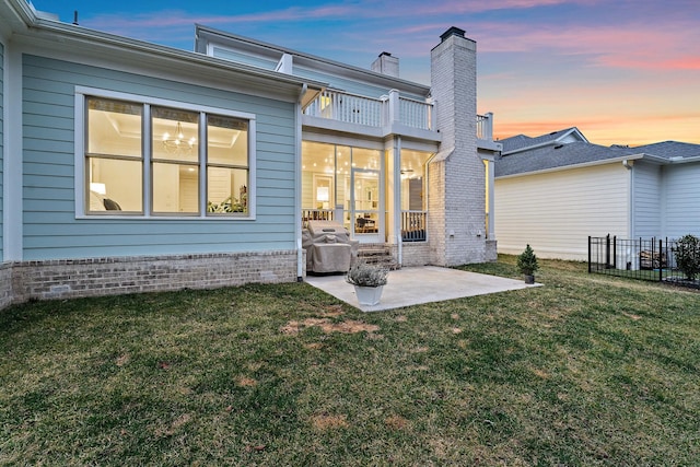 back house at dusk with a patio and a lawn